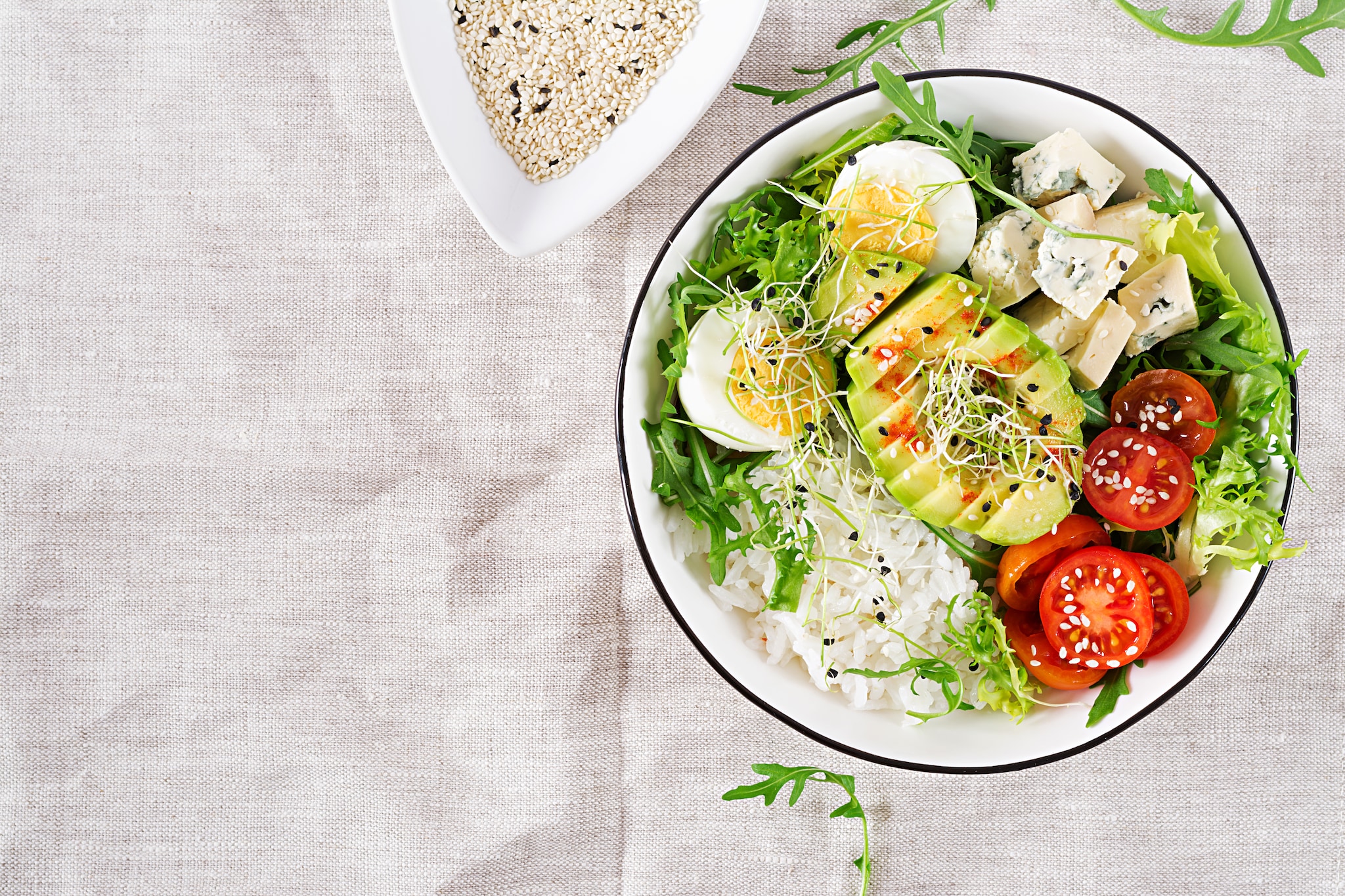 healthy green vegetarian buddha bowl lunch with eggs rice tomato avocado blue cheese table