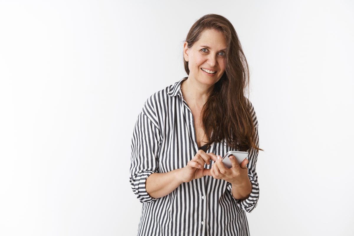 charming middle aged woman holding smartphone being distracted from using mobile phone 16753943893x2 GF7fwd