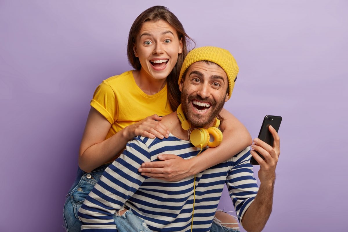 photo young boyfriend girlfriend have fun together man gives piggyback ride female use mobile phone laugh joyfully isolated purple wall happy bloggers 16769641753x2 Jh7BkJ